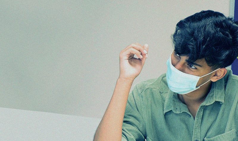  man wearing a mask sits at a desk, focused on his work in a well-lit office environment.