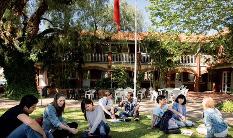 Several individuals are seated on the grass, with a building visible in the background, creating a relaxed atmosphere.
