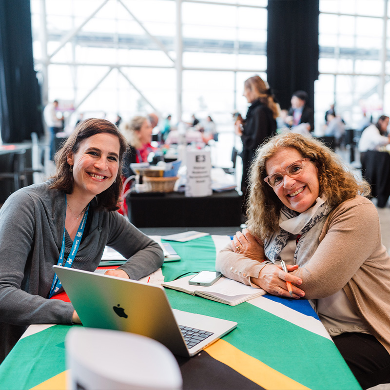 Two women engaged in discussion at a table, with a laptop open between them.